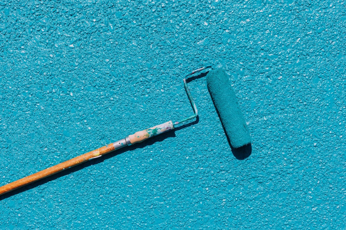 Close-up of a paint roller applying teal paint to a wall